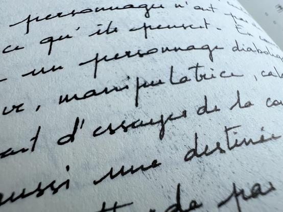 Close-up of a notebook page with handwriting in black. The ink has smudged and there are tiny dots of ink between the words. 