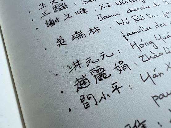Close up of a notebook page with a list of names in Chinese written with a black ink. The ink has smudged at some places around Chinese characters. 