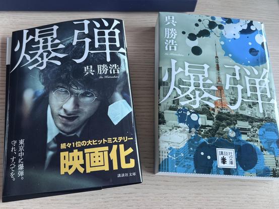 A Japanese book on the right and a book cover on the left are lying on a table. They have the same title but not the same cover design. The empty cover advertises for the film adaptation of the novel and displays a scene from the film. 