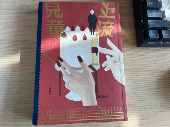 A book written in Traditional Chinese is on a wooden table. The cover shows two manicured hands reaching for a cake with a faceless child standing on it. 