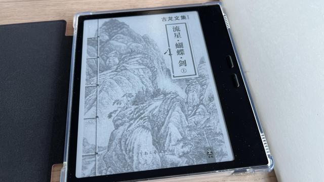 E-reader with a protective case opened on a table. The screen displays the cover of a book in Chinese with a traditional binding and an ink painting of mountains as illustration.