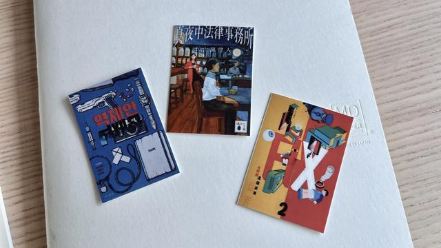 Three small sticker sheets printed with book covers are displayed on a notebook. The covers are colourful and in different languages. 