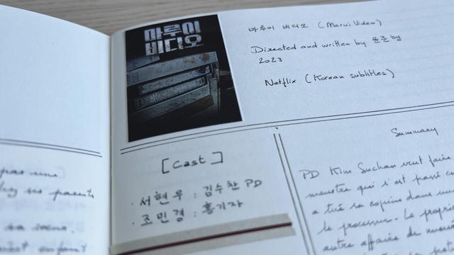 Top part of the right page of a notebook. On the very top left corner of the page, there’s a film poster with the title Marui Video in Korean and VHS piled up under the title. Near the poster are some information about the film “Marui Video, directed and written by Yoon Joon-Hyeong, 2023, Netflix (Korean subtitles)”. Underneath there’s the cast and a summary written in French, but most of it is outside the frame.